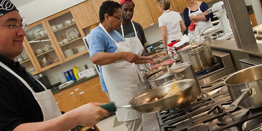 Three cooking class participants cooking at two of the stoves in our kitchen