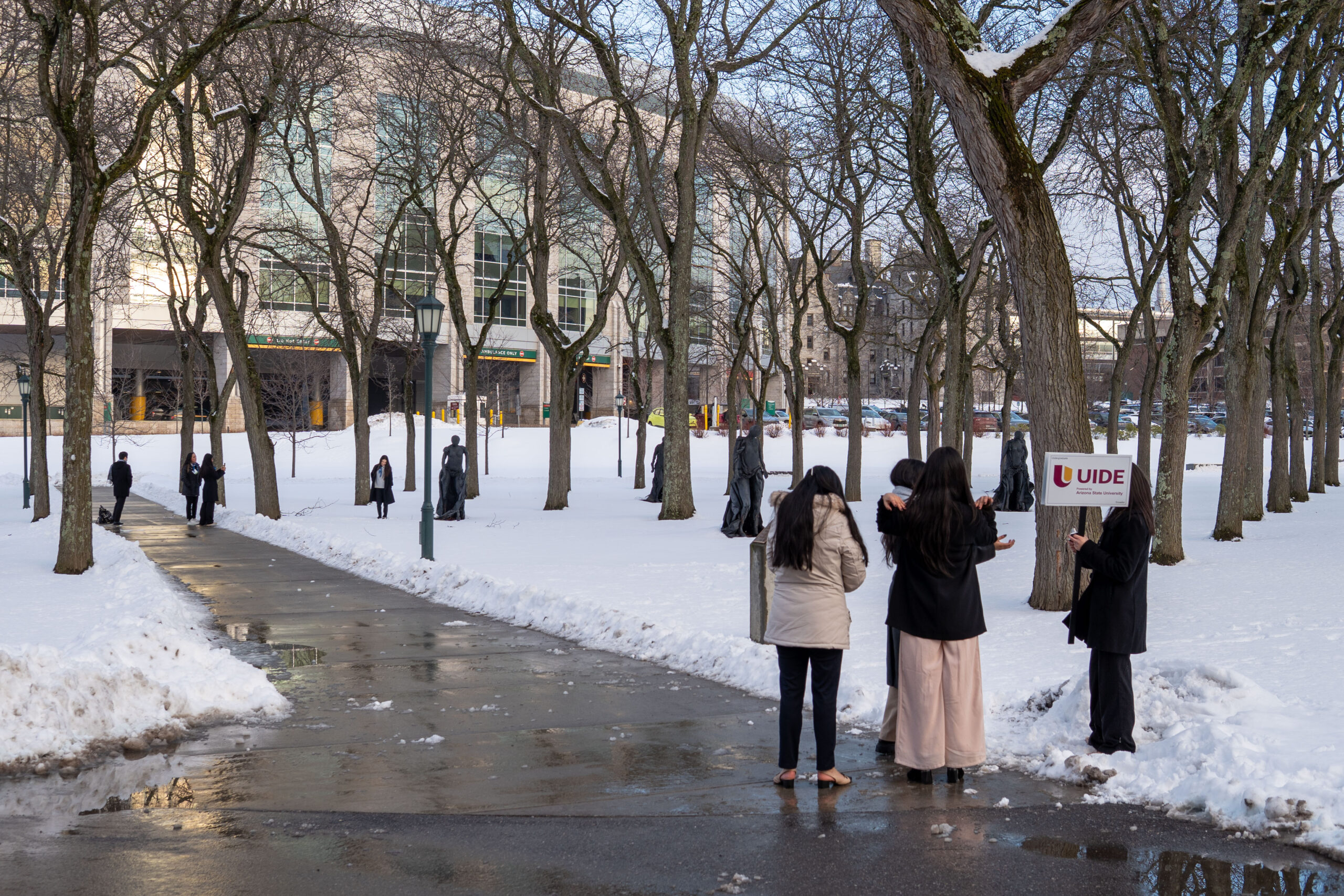 Students stand outside on a walkway surrounded by snowy grounds and buildings