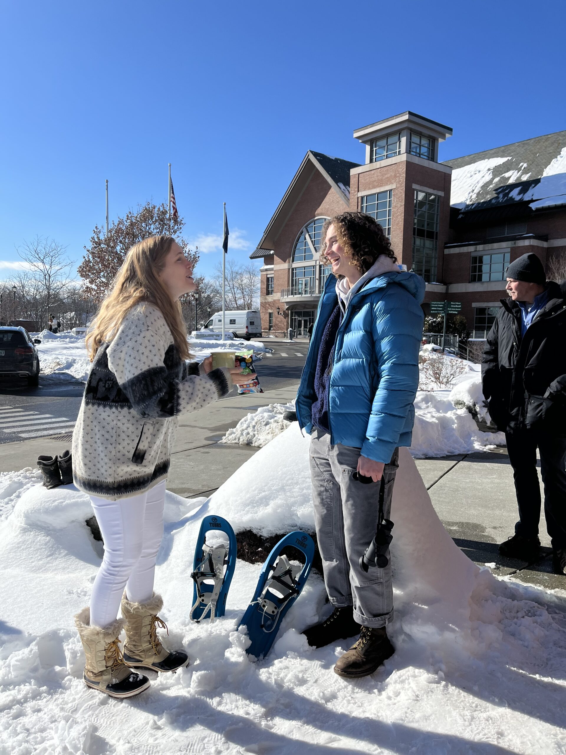 Two students talking while standing outside in snow boots.