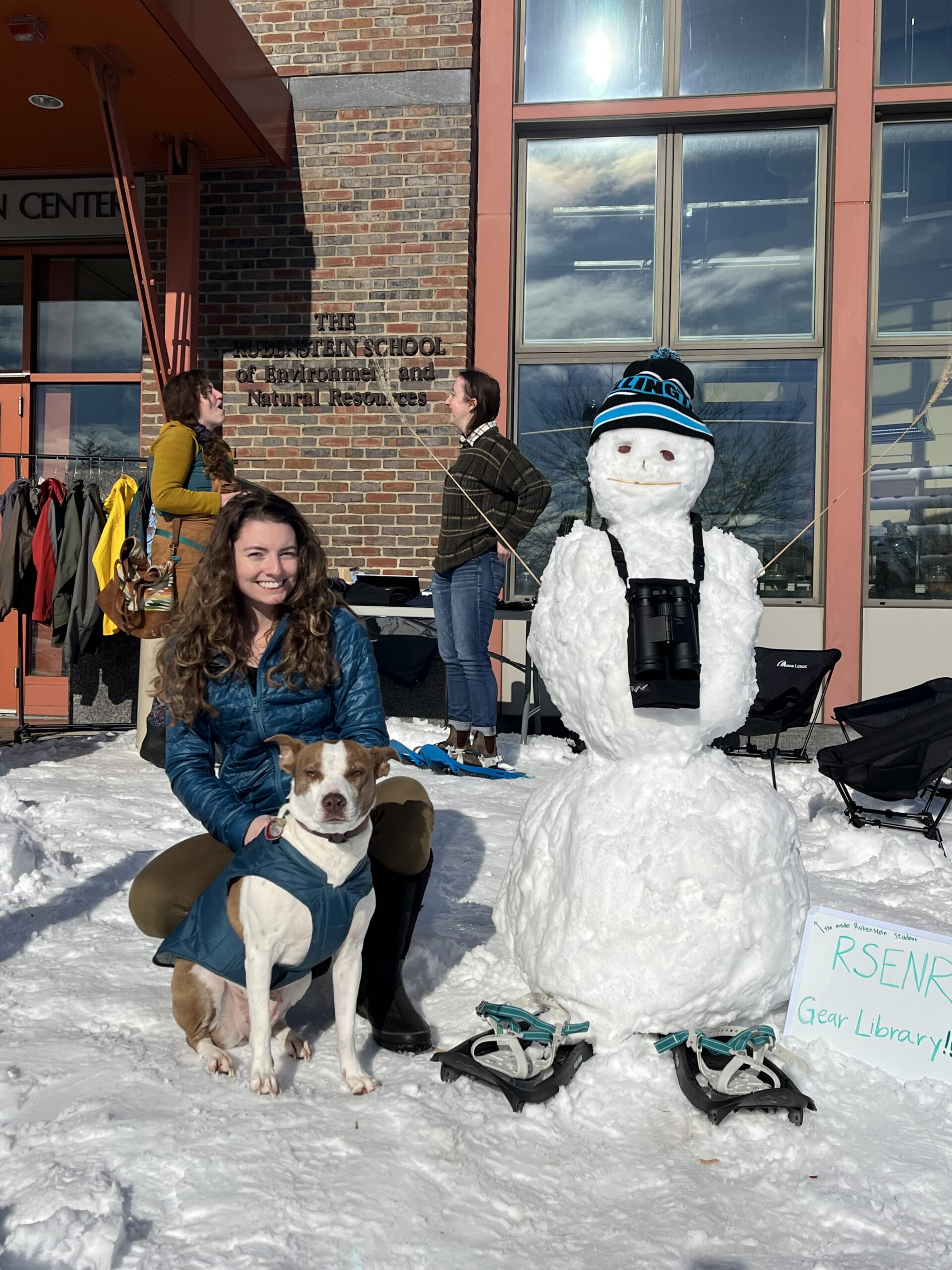 Brittany Claussen and her dog Ginny standing next to a snowperson wearing snowshoes and binoculars