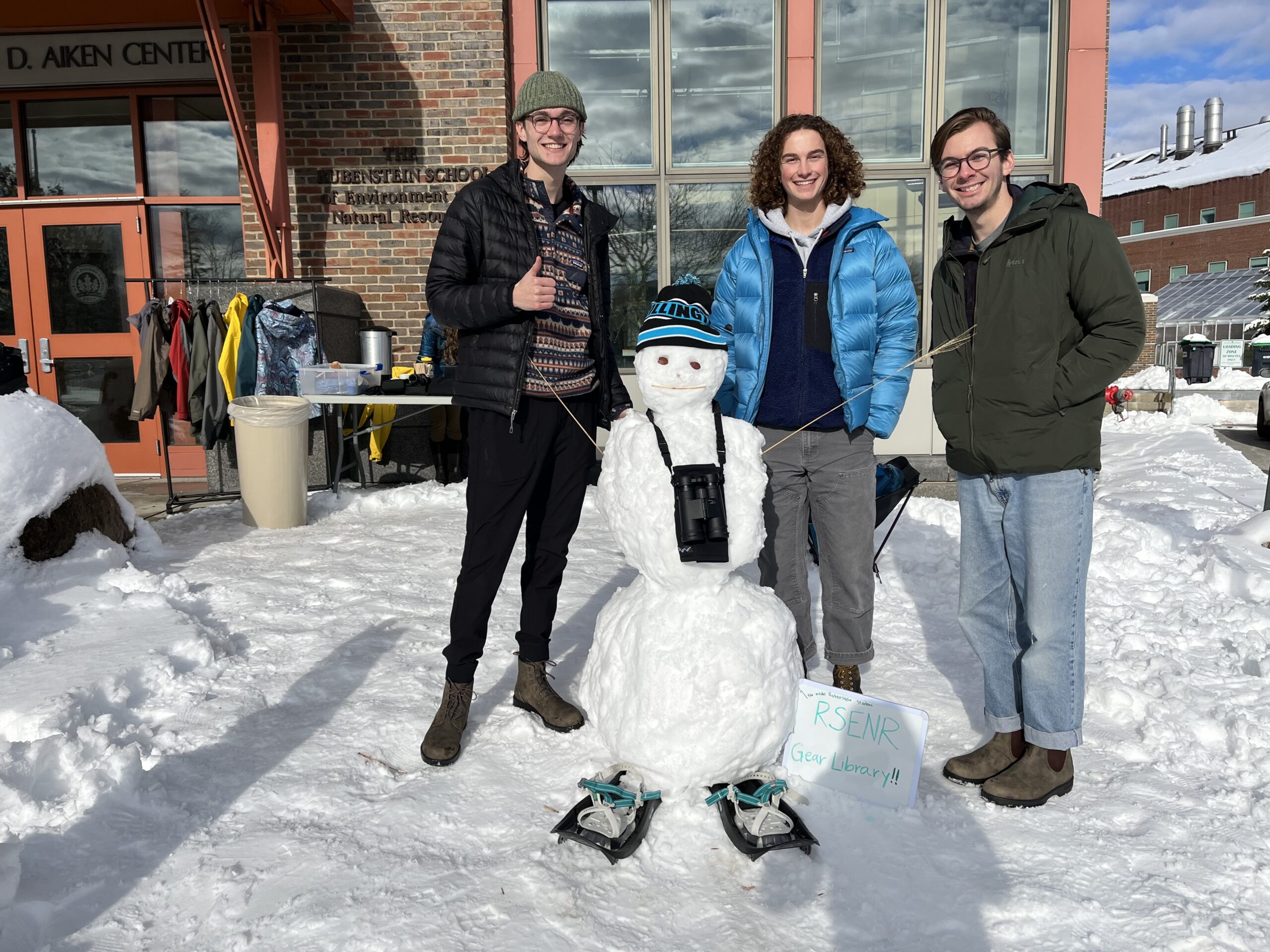 Students standing with a snow person wearing snowshoes and binoculars