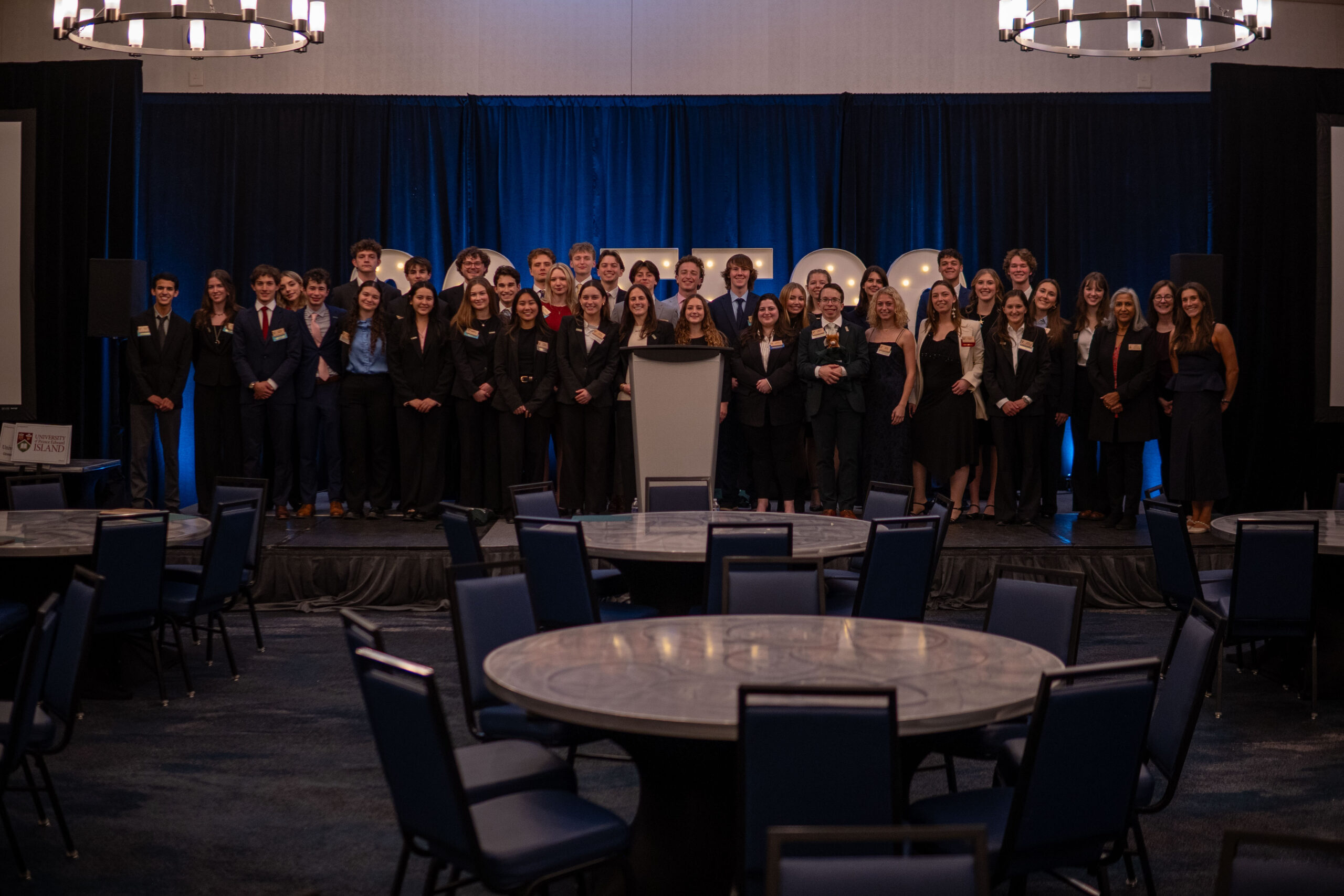 A large group of students dressed in business attire stand on stage